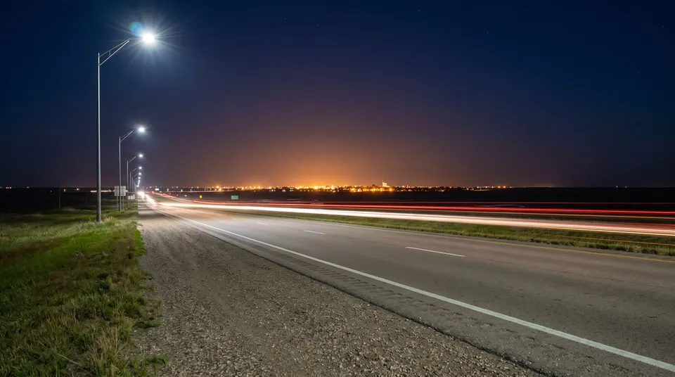 Highway at night with car light trails near a small city